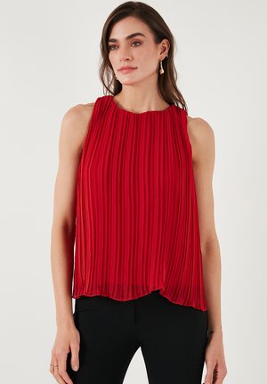 Red pleated sleeveless top with a round neckline, featuring a flowy silhouette and a lightweight texture. Paired with black fitted pants.