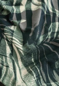Puuvillane kangas rohelise ja halli abstraktse lehemustriga, millel on erinevad tekstuurid ja kihilised kujundid, veidi kortsus.
