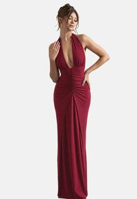 Robe halter maroon avec un décolleté en V profond et des détails froncés, silhouette ajustée et longueur maxi dans un tissu doux et extensible.
