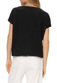 Czarna bluzka krótki rękaw o luźnym kroju i fakturowanej tkaninie. Posiada lekko zaokrąglony dekolt i sięga tuż poniżej talii.