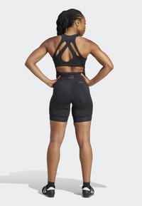 Black athletic wear featuring a sleeveless top with a cutout back and high-waisted shorts. Smooth texture, fitted design, minimal branding.