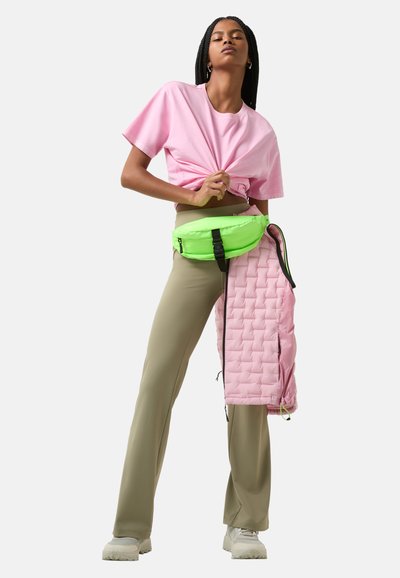 Roze cropped t-shirt, olijfgroene broek, neongroene heuptas en lichtroze gewatteerde bovenkleding met ritsen. Textuurcontrast in de stof.