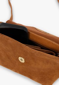 Braune Wildleder-Umhängetasche mit Futter aus Stoff, ausgestattet mit einem goldenen Druckknopfverschluss und einem teilweise sichtbaren Smartphone im Inneren.