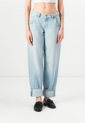 Lichtblauwe, high-waisted denim jeans met een ontspannen pasvorm, omgeslagen manchetten en gevlochten details op de tailleband. Gecombineerd met zwarte loafers.
