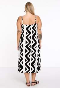 Robe longue noir et blanc avec un motif géométrique, dotée de fines bretelles et d'une coupe décontractée, fabriquée à partir d'un tissu doux.