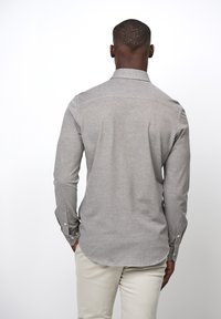 Camicia con maniche lunghe e bottoni di colore grigio chiaro, realizzata in tessuto morbido, con colletto classico e polsini abbottonati con orlo curvo.
