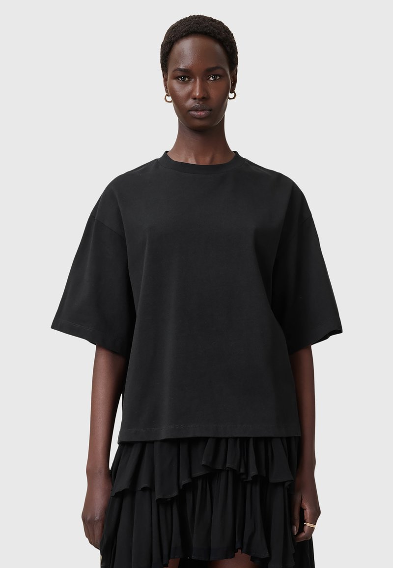 Sort oversized T-shirt lavet af bomuld, med korte ærmer og lige snit. Kombineret med en voluminøs sort nederdel.