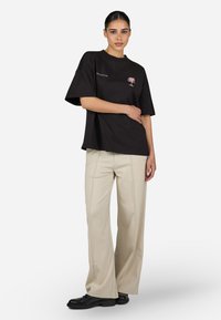 Camiseta negra de gran tamaño con bordado de palmera rosa, combinada con pantalones de pierna ancha color crema y zapatos negros. Tejido suave, ajuste casual.