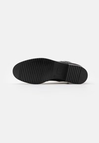 Suela de zapato negra con patrón de estrías horizontales, talla 39, fotografiada sobre un fondo blanco liso.