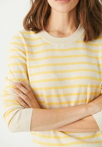 Pull beige clair avec des rayures jaunes, col rond côtelé et manches longues. Texture en maille douce avec une coupe décontractée.