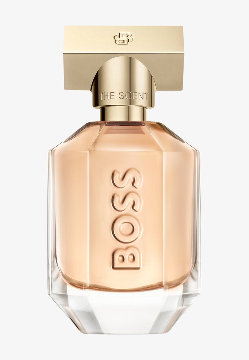 Flacon de parfum en verre transparent avec liquide couleur pêche, bouchon rectangulaire doré et "BOSS" embossé verticalement à l'avant.