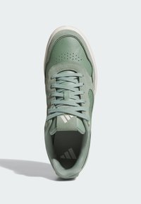 Zelené kožené tenisky s perforacemi, šněrováním a texturovanou bílou podrážkou. Na jazyku je logo se třemi pruhy.