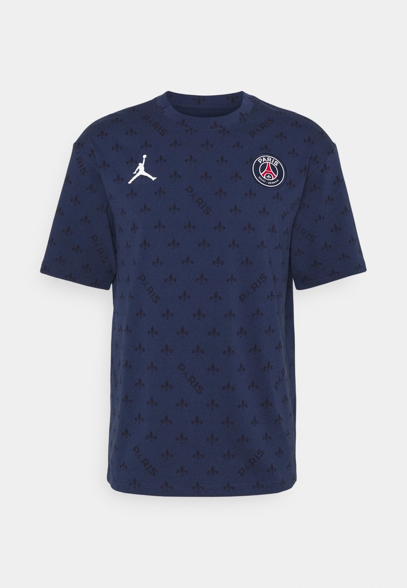 T-shirt bleu marine Paris Saint-Germain avec motif fleur de lys, logo Jumpman blanc sur la poitrine droite et emblème PSG sur la poitrine gauche.