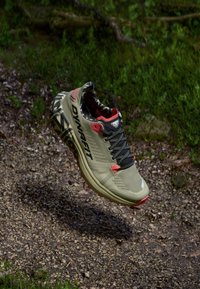 Ελαφριά αθλητικά παπούτσια τρεξίματος σε ελαιόχρωμο με κόκκινες λεπτομέρειες, αναπνεύσιμο άνω μέρος από διχτυωτό υλικό, υφή σόλας και μοτίβο παραλλαγής εσωτερικά.