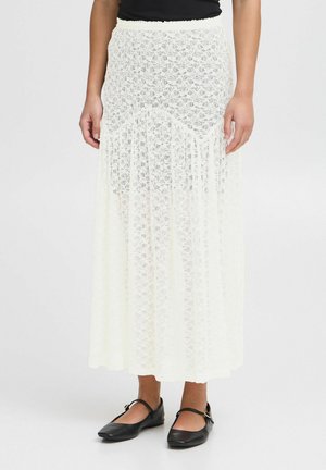 Maxi skirt made of white lace with a flowy design. Features a scalloped waistband and a layered hem, worn with black flat shoes.