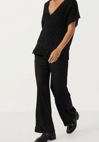 Pull noir à manches courtes et col en V avec une finition texturée et scintillante ; assorti à un pantalon noir à jambes larges et des chaussures noires à lacets.