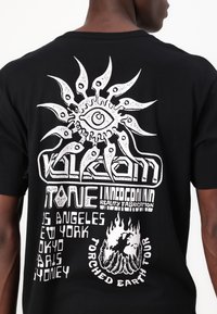 Camiseta negra con diseño gráfico en blanco que presenta un motivo de sol y texto con el nombre de ciudades. El material parece ser algodón; el diseño es audaz y llamativo.