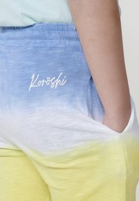 Ľahké joggingové nohavice s prechodom z modrej na žltú, vyrobené z mäkkého materiálu, s elastickým pásom a bočnými vreckami. Zobrazené logo.