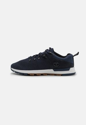 Zapatilla deportiva de color azul marino con parte superior de punto, acentos de ante, una mediasuela blanca y una suela exterior de goma texturizada con un logotipo de marca en el costado.
