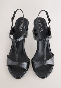 Sandale negre slingback din piele texturată, cu barete încrucișate, tălpi plate și cataramă de ajustare la gleznă.