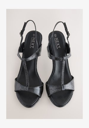 Zwarte slingback sandalen van getextureerd leer, voorzien van gekruiste bandjes, platte zolen en een verstelbare enkelgesp.