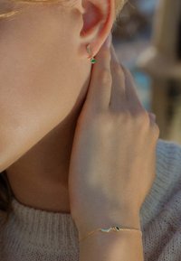 Goldohrringe mit Smaragdakzenten im Design einer Mondsichel. Ein passendes Goldarmband mit einem Smaragddetail an einer zarten Kette.