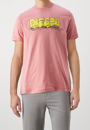 T-shirt en coton rose à manches courtes, présentant un graphisme "DIESEL" jaune et noir déformé sur la poitrine. Design simple avec col rond.
