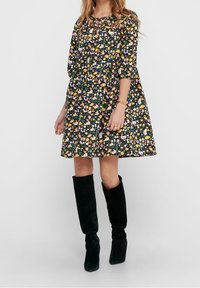 Vestido de estampado floral con fondo negro, que presenta un corte holgado, mangas tres cuartos y botas de ante negras hasta la rodilla.
