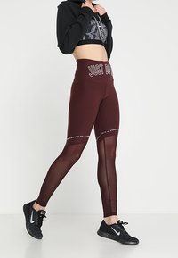 Leggings bordeaux a vita alta con pannelli in rete e la scritta "JUST DO IT" all'altezza della vita. Abbinati a sneakers nere. Progettati per l'abbigliamento sportivo.