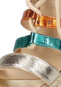 Sandalias de tacón alto metálicas con tiras en plata, azul verdoso y naranja. Las superficies texturizadas y los detalles trenzados realzan el diseño.