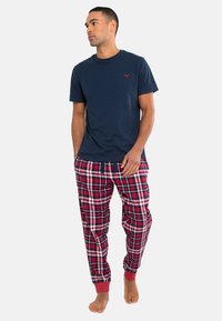 Navy katoenen t-shirt met een klein rood logo, gecombineerd met rode en navy geruite pyjamabroek met elastische boorden en een relaxte pasvorm.