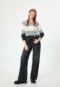 Grau-weiß gestreifter Pullover mit strukturiertem Finish, kombiniert mit weiten schwarzen Jeans und klobigen schwarzen Schuhen. Einfaches und modernes Design.