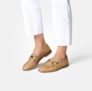 Woven tan loafers with a flat sole, featuring a gold-tone hardware detail and a textured finish. Paired with white, frayed hem jeans.