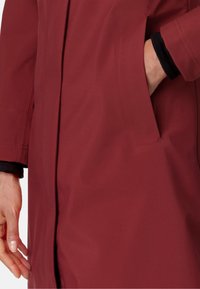 Giacca bordò con una texture liscia, dotata di una tasca laterale e dettagli neri sui polsini. Il design è minimalista con linee pulite.