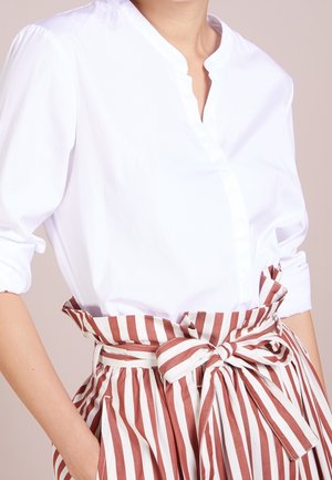 Witte overhemd met kraag, gecombineerd met een rood-wit gestreepte hoge taille rok met een strikceintuur.