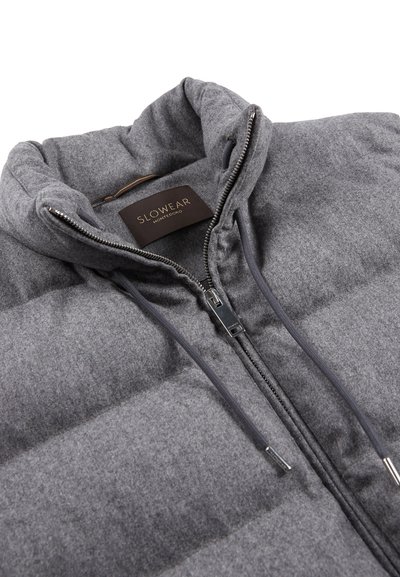 Grau gefütterte Jacke mit hohem Kragen, gestepptem Muster und Reißverschluss. Verfügt über ein braunes Markenetikett mit "SLOWEAR" und silbernem Zipper.