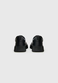 Ein Paar schwarze Low-Top-Sneaker mit dicken, gerippten Sohlen, von hinten auf einem schlichten weißen Hintergrund dargestellt.