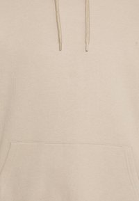 Beige huva med en mjuk textur, framficka i kängurustil och dragsko på huvan. Enkelt design utan mönster eller utsmyckningar.