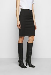 Falda lápiz negra con un diseño ajustado y costuras laterales, combinada con botas de cuero negro de tacón alto hasta la rodilla. Textura suave y mate en todo su diseño.