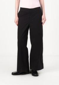 Calças largas pretas feitas de um tecido macio. Apresentam dois bolsos laterais, uma cintura plana e uma textura suave sem padrões visíveis.