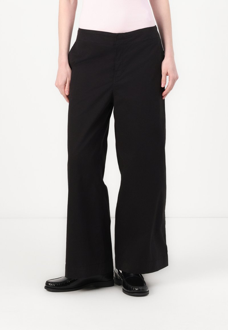 Calças largas pretas feitas de um tecido macio. Apresentam dois bolsos laterais, uma cintura plana e uma textura suave sem padrões visíveis.