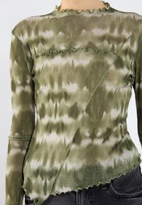 Long-sleeve top in green tie-dye pattern, featuring ruffled edges and an asymmetrical design, made of lightweight, textured fabric.
