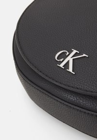 Borsa a tracolla nera in pelle con una finitura testurizzata. Presenta un accento in logo argento e bordi cuciti. Design compatto con superficie liscia.