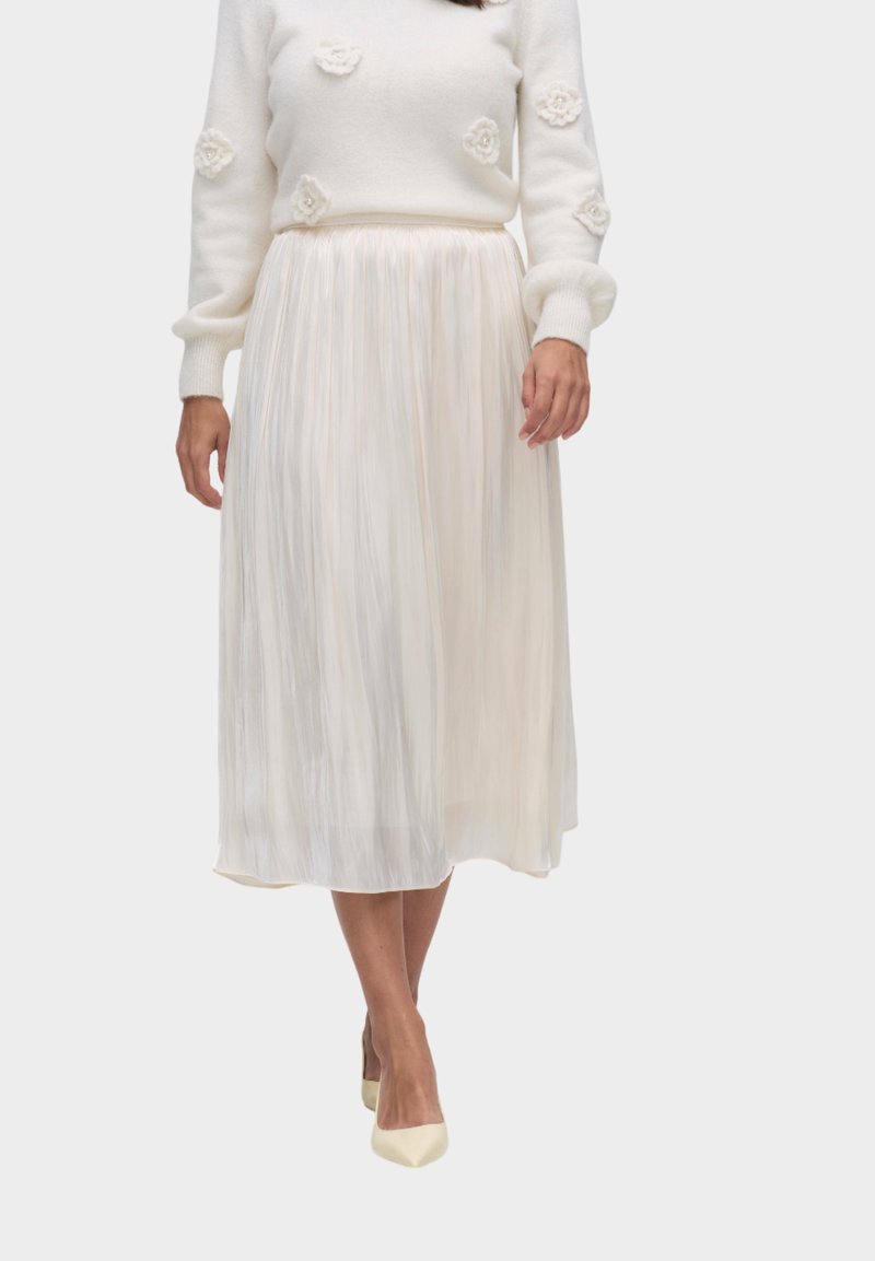 Witte, gestructureerde trui met bloemaccenten; ivoorkleurige geplooide midi-rok; slanke silhouet; beige puntige hakken.