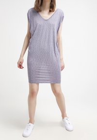 Vestito viola, con maniche corte, dalla lunghezza al ginocchio e scollo a V, realizzato in tessuto leggero con un leggero motivo testurizzato. Indossato con sneakers bianche.