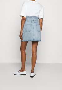 Blå denim mini kjol med bälte i midjan, två bakfickor och rak skärning, i kombination med en vit t-shirt och vita loafers.