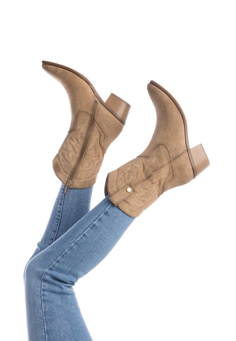 Botas de cowboy de ante en tono marrón con punteras puntiagudas y tacón cuadrado. Presentan detalles de costura y un zipper lateral expuesto, con acentos decorativos.