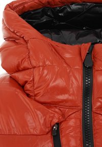 Giacca imbottita rossa isolante con una texture lucida, collo alto e cerniera nera. Interno nero con dettagli imbottiti trapuntati.