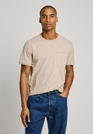 Lys beige kortærmet t-shirt med rund halsudskæring og en brystlomme, parret med mørkeblå denim jeans. Glat fabrickvalitet.