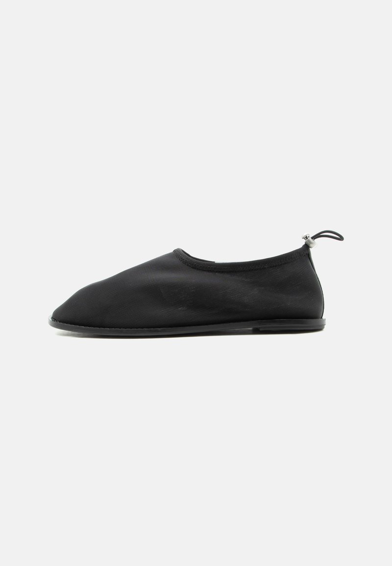 Chaussure en tissu noire à enfiler avec semelle plate et boucle élastique réglable au talon, vue de côté extérieur sur fond blanc.
